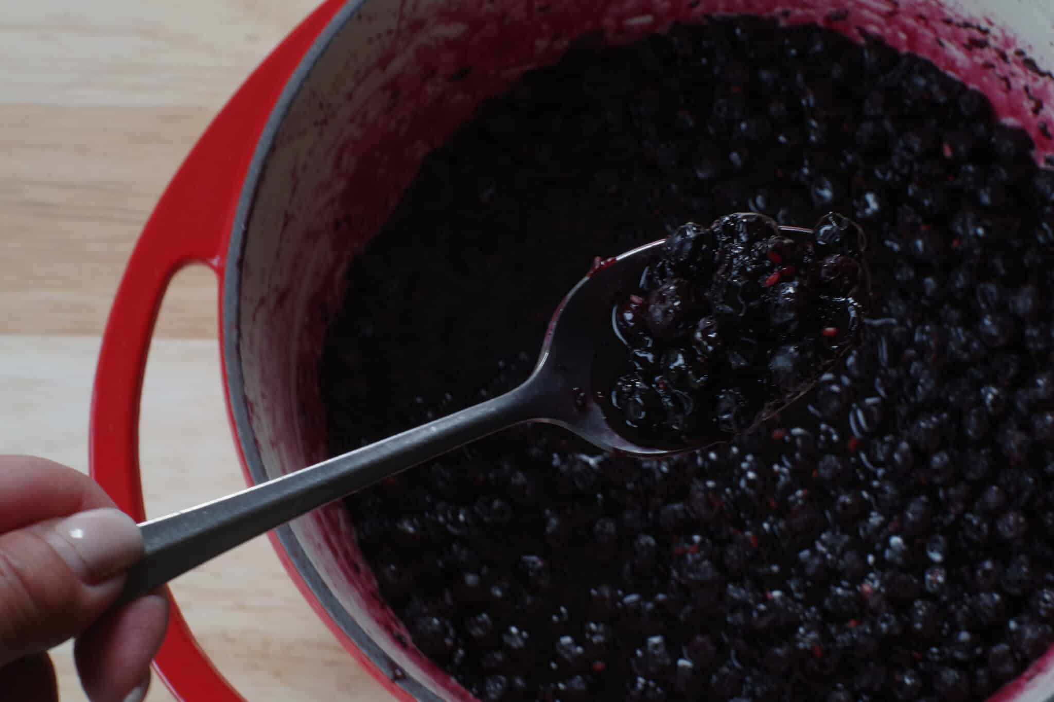 Saskatoon berry jam (still hot) being held up on a spoon.