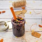 Saskatoon Berry Pie Jam in a glass jam jar with a cinnamon stick in the jar and lemon zest, surrounded by labels, and string.