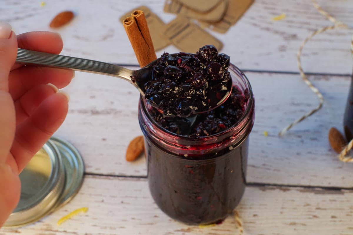 Saskatoon Berry Pie Jam being held up on a spoon over a jar of Saskatoon Berry Jam.