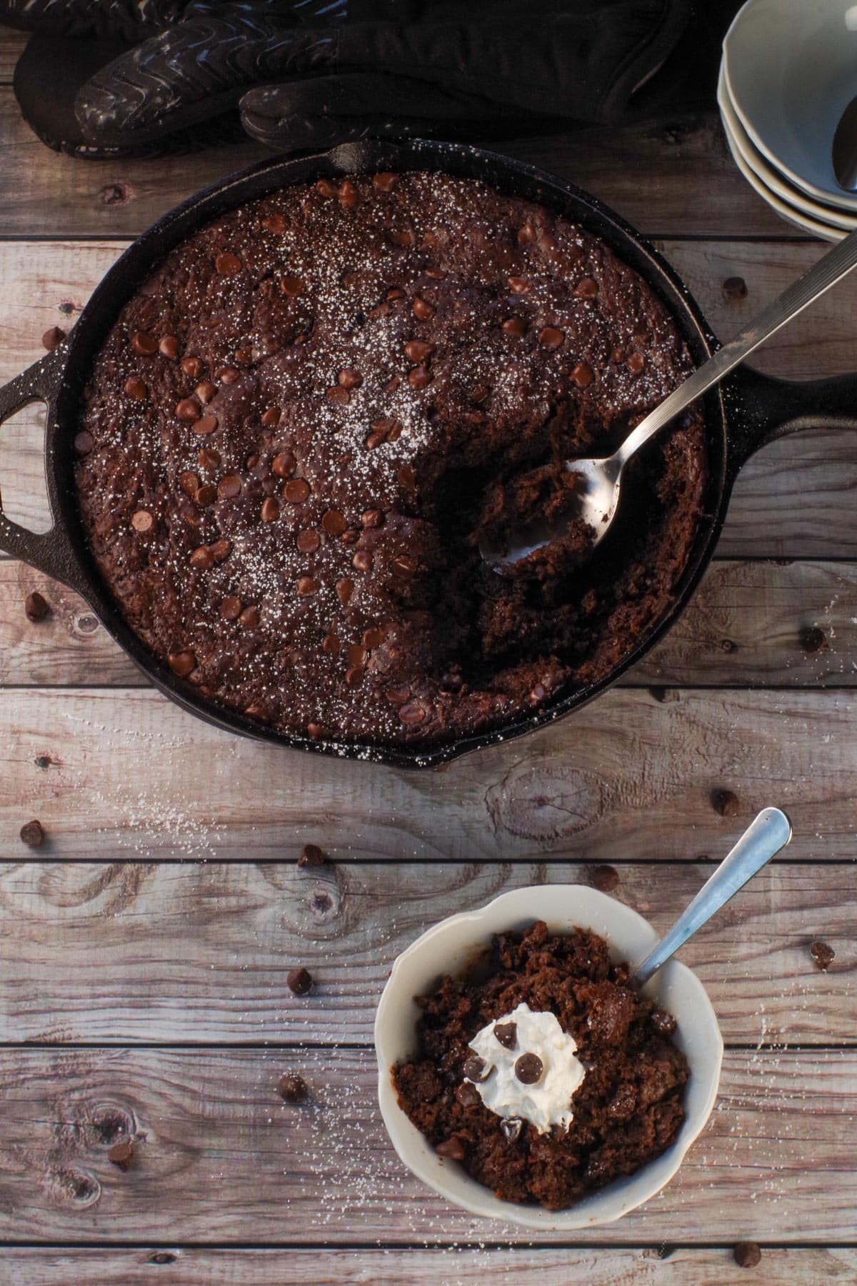 Overhead view of Chocolate Zucchini Spoon Cake in a small white flour blow with more cake in the cast iron skillet in the background.
