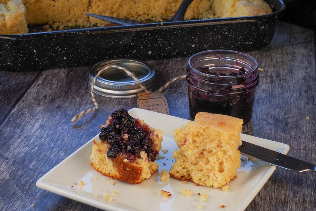Saskatoon Berry jam on cornbread on a plate with a jar of jam behind the plate.