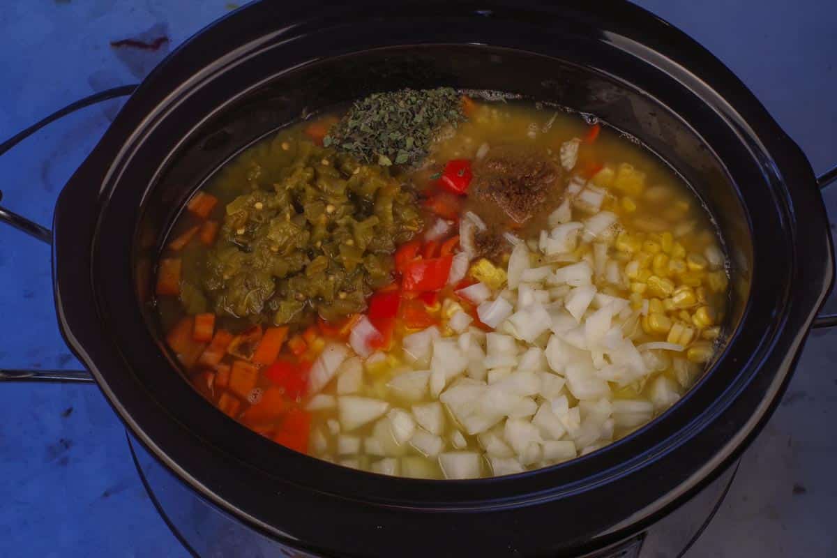 Chicken broth, raw chicken breasts (whole), 2 cans of white kidney beans (only 1 drained), red pepper, fresh corn, green chilies, onion, garlic, cumin, oregano, chili powder, salt and pepper and jalapenos added to the crockpot.