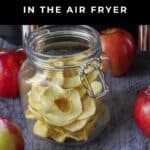 A jar of dehydrated apple rings with 4 fresh apples around the jar.