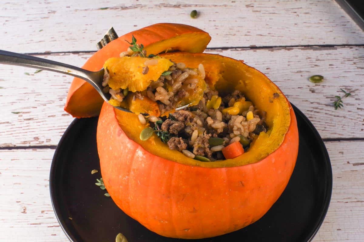 Slow Cooker Dinner in a Pumpkin being held up on a spoon over the filled pumpkin.