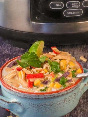 Healthy Creamy Crockpot White Chicken Chili in a bowl, in front of a slow cooker.