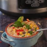 Healthy Creamy Crockpot White Chicken Chili in a bowl, in front of a slow cooker.