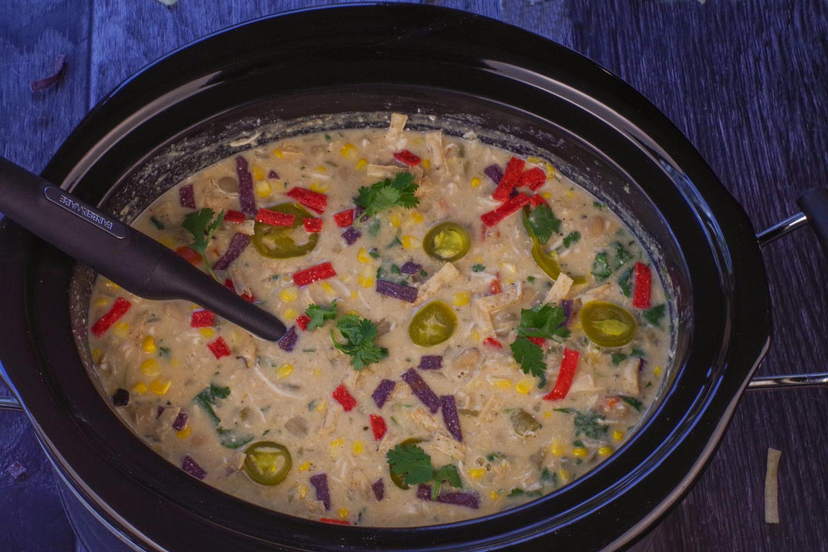 Healthy Crockpot White Chicken Chili in the slow cooker with a black ladle.
