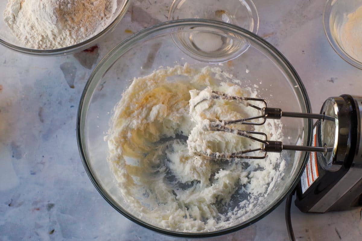 Shortening and sugar being beaten together in glass bowl with an electric mixer.
