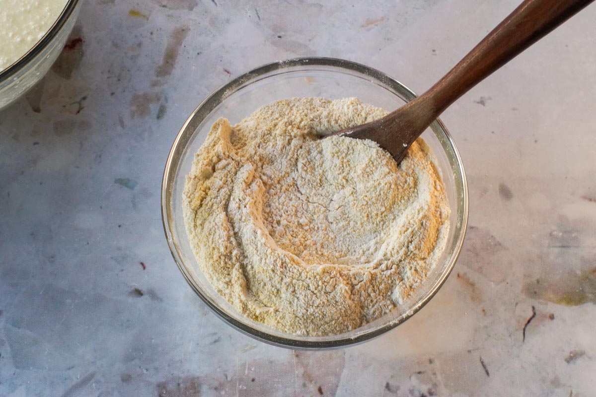 Dry ingredients mixed together in medium glass bowl with wooden spoon.