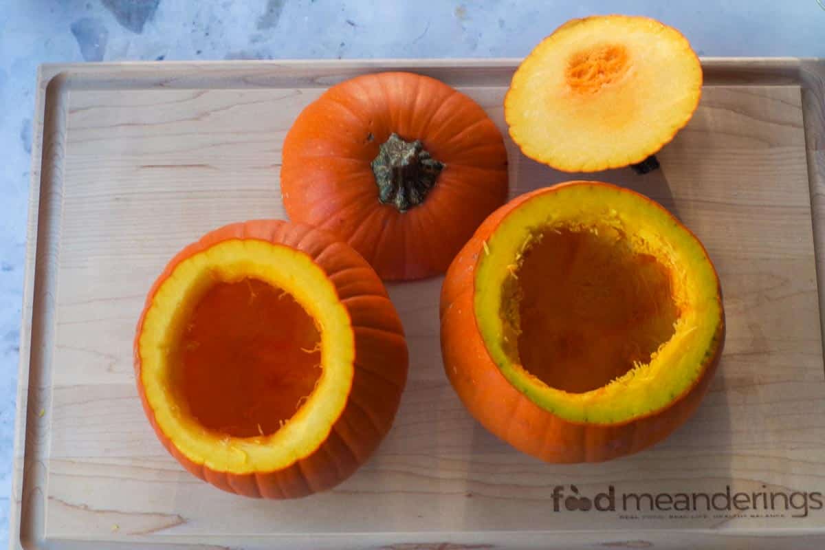 2 small sugar pumpkins on a wooden cutting board with tops cut off and seeds and pulp scooped out..