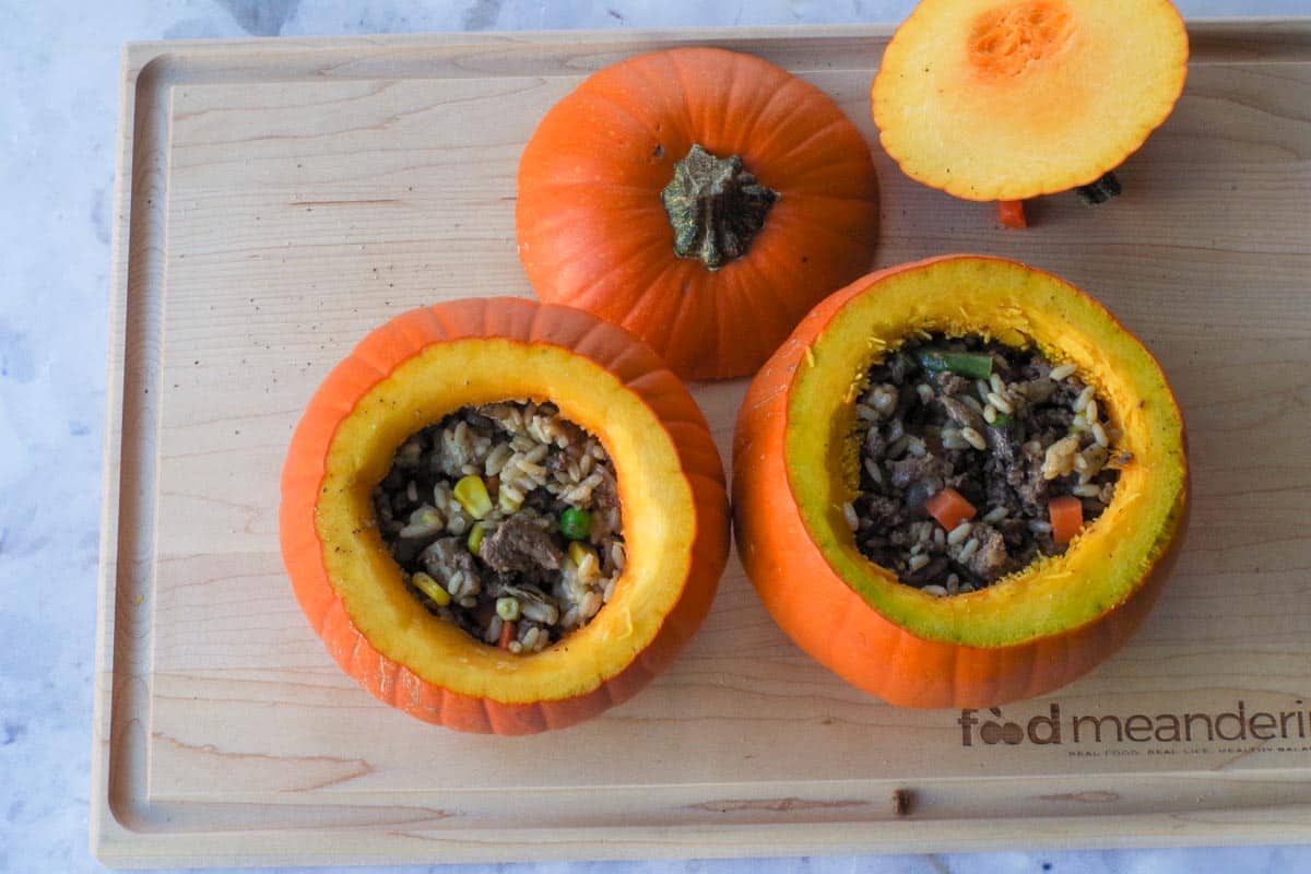Beef and rice mixture packed into the pumpkins on a wooden cutting board.