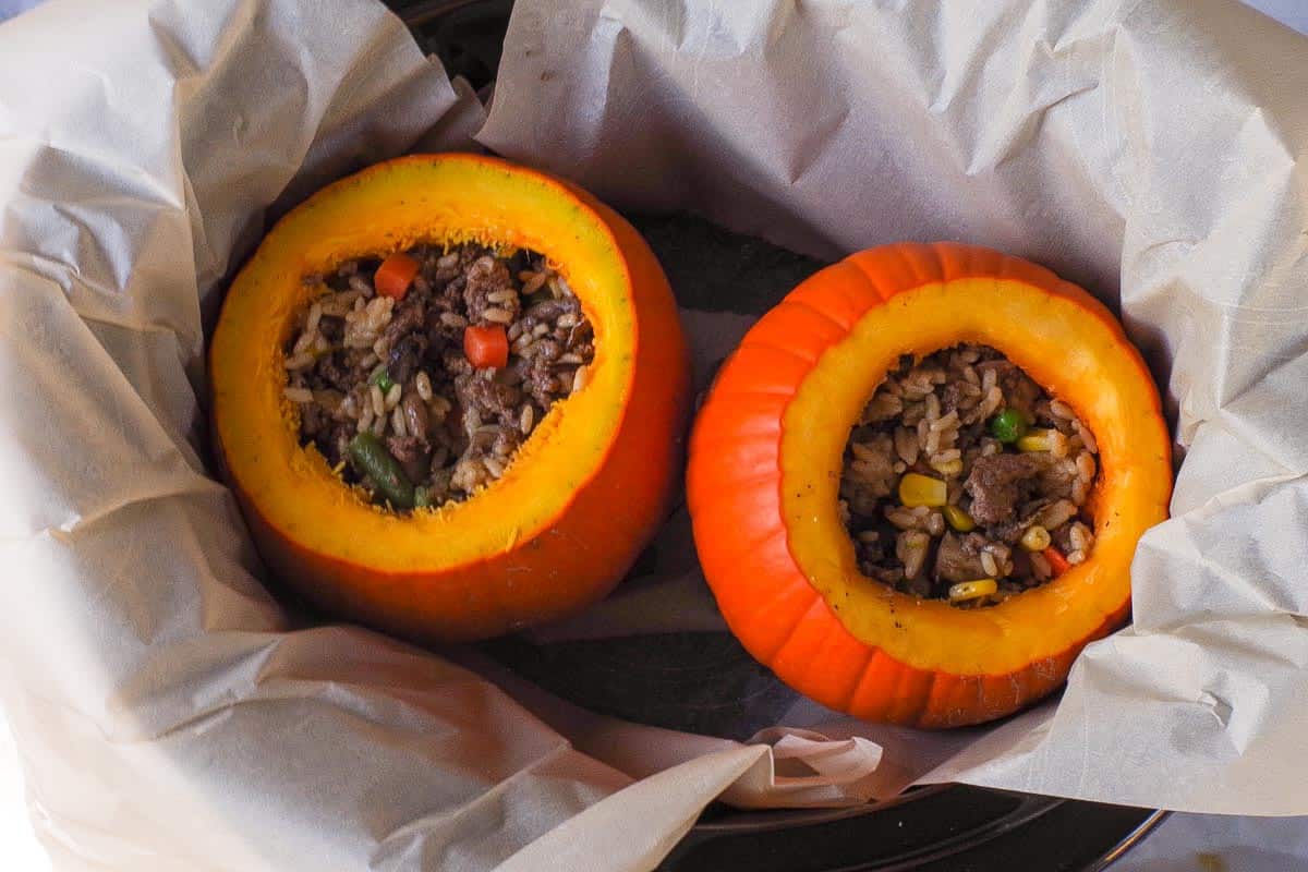 Filled pumpkins placed in slow cooker on top of parchment sling.