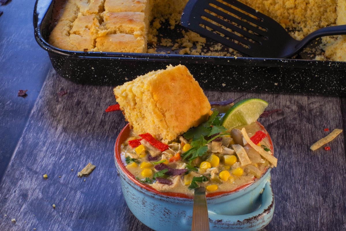 A bowl of Slow Cooker White Chicken Chili with a piece of cornbread in the bowl.